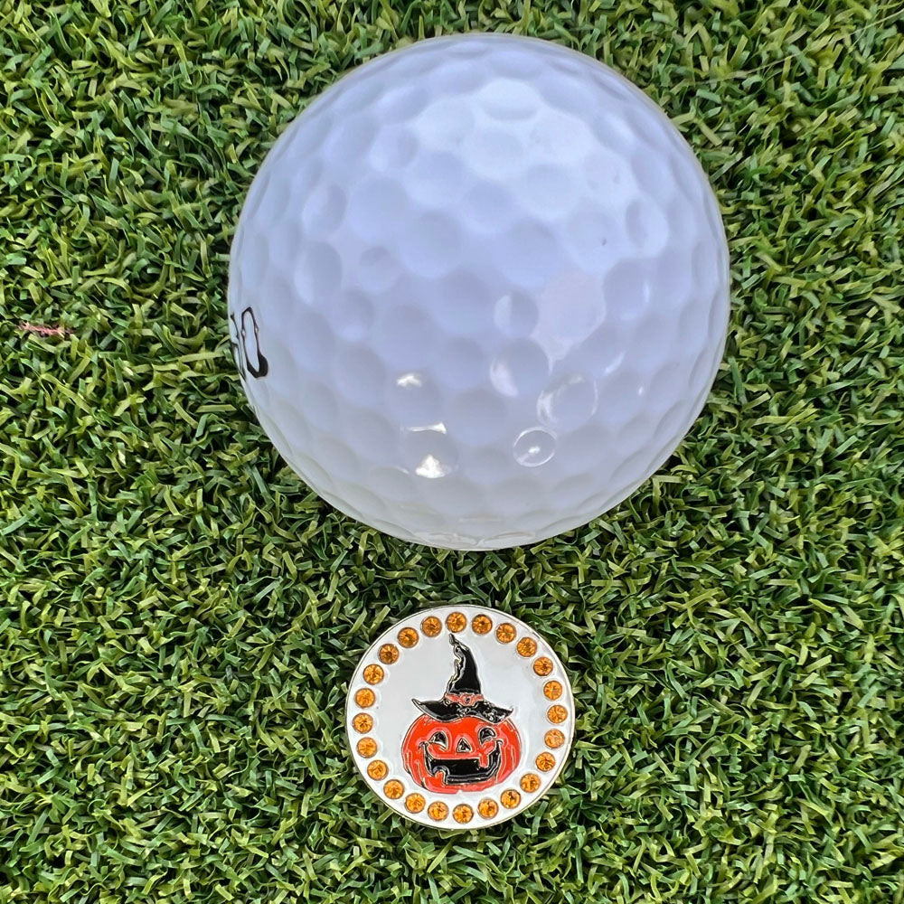 Golf ball on grass with a Halloween-themed pumpkin golf ball marker.