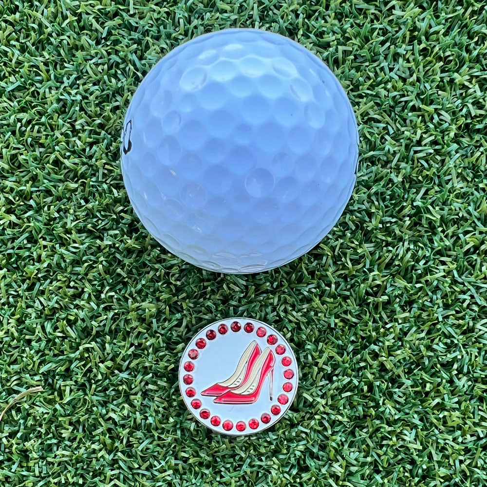 Golf ball on grass with a decorative golf ball marker featuring red high heels.