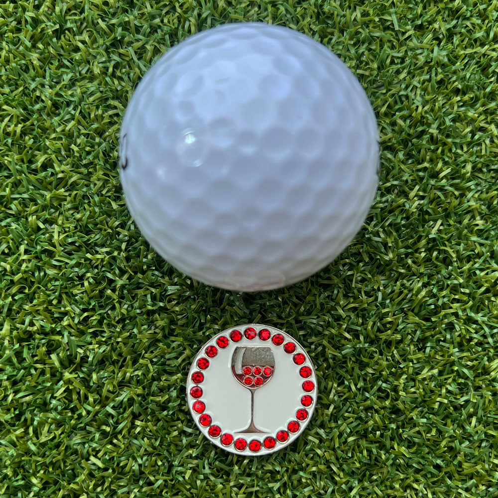 Golf ball on grass with a decorative golf ball marker featuring a red wine glass design.