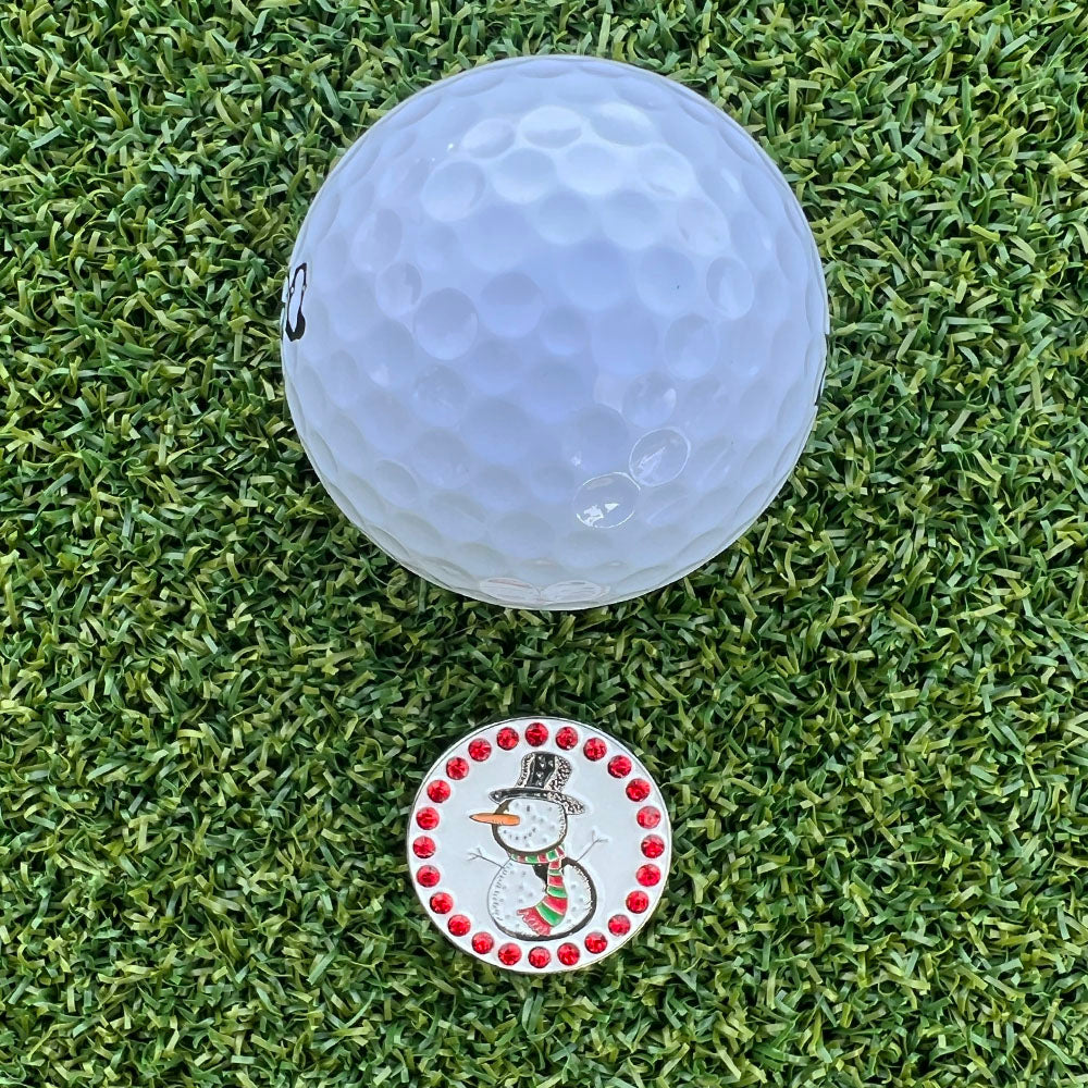 Golf ball on a grass surface with a snowman-themed golf ball marker.