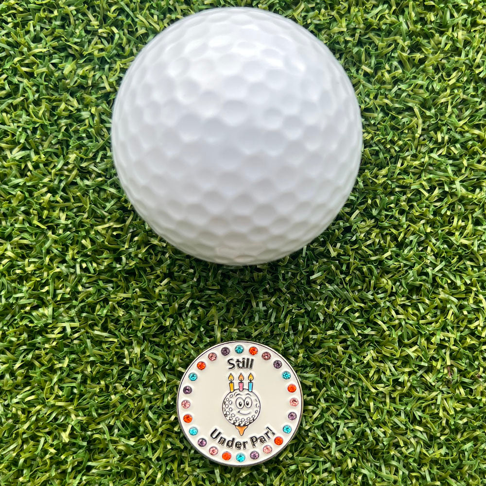 Women's golf ball on grass with a decorative birthday themed golf ball marker below it