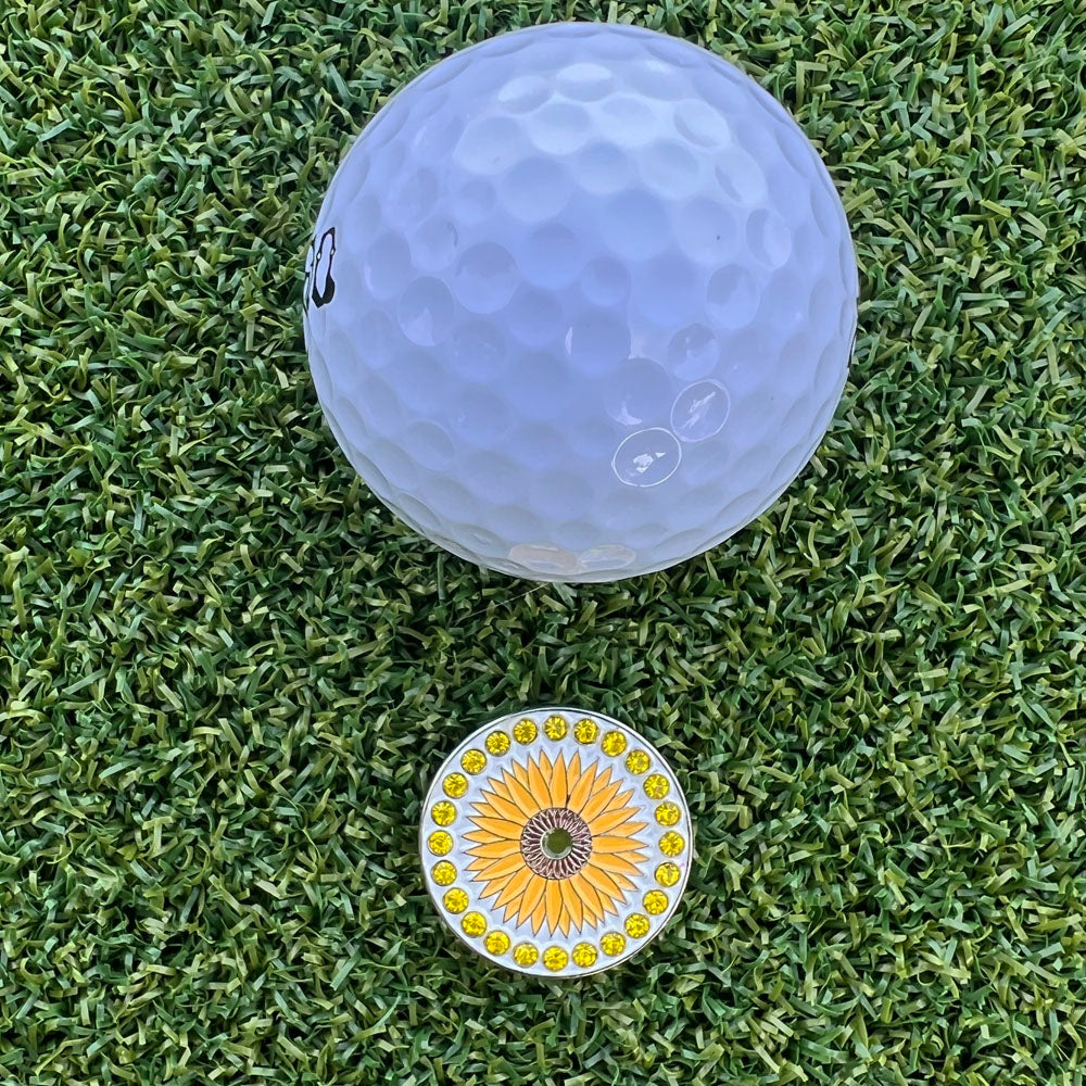 White golf ball on green grass with a bling golf ball marker featuring a sunflower design.