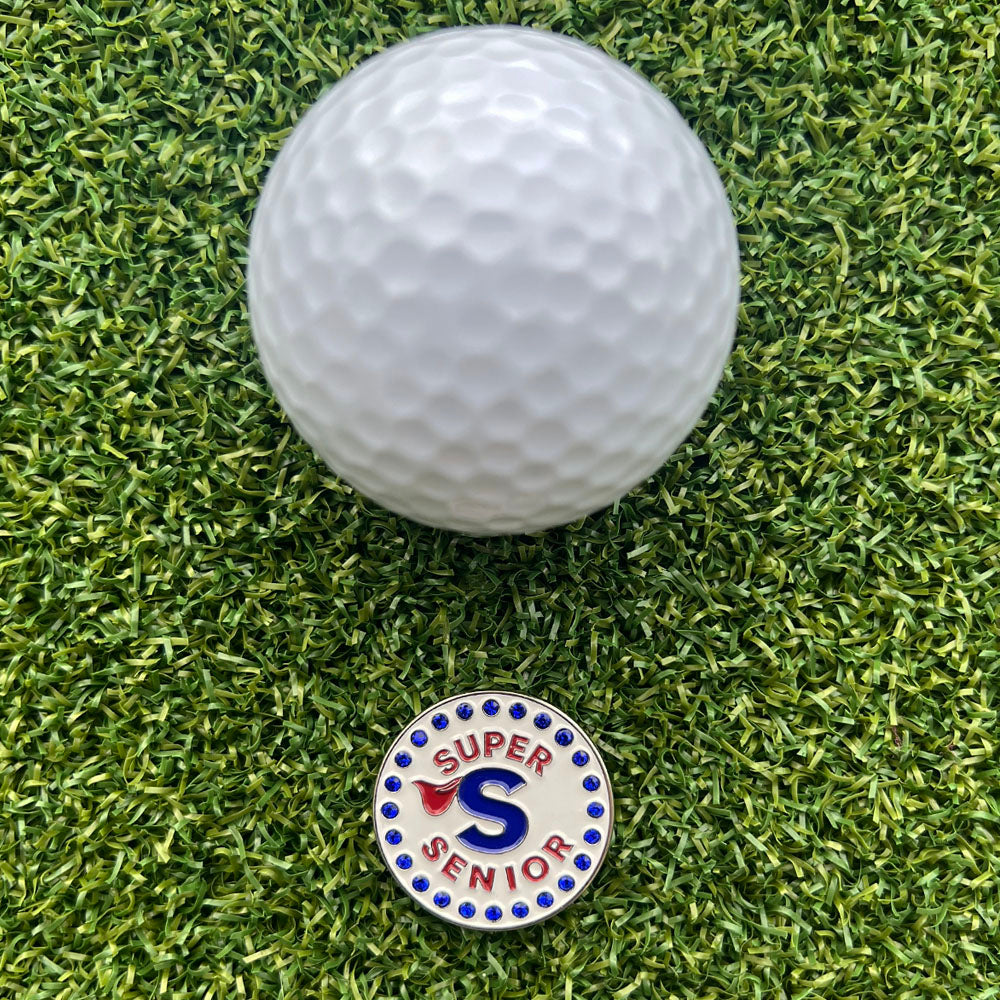 Golf ball on green grass with a 'Super Senior' bling golf ball marker in front