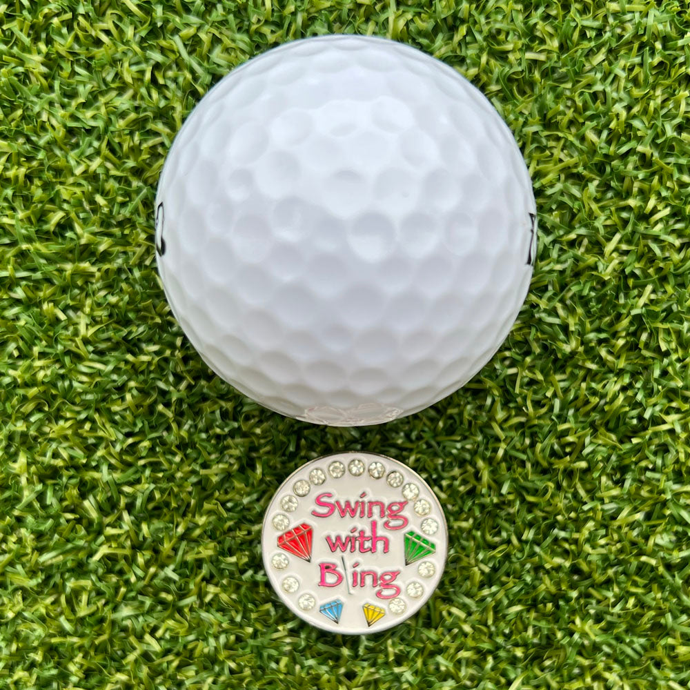 Golf ball on grass with a colorful ball marker with 'Swing With Bling' text in pink