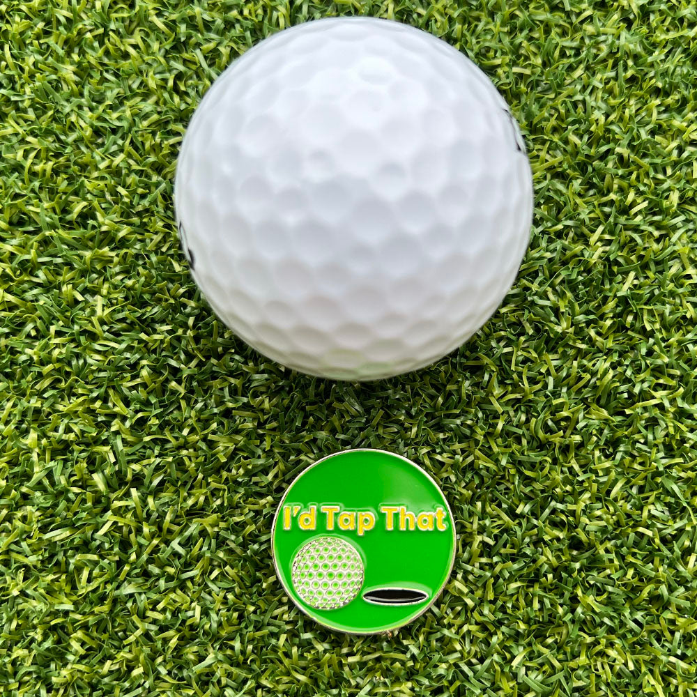 Golf ball on green grass with a 'I'd Tap That' golf ball marker.