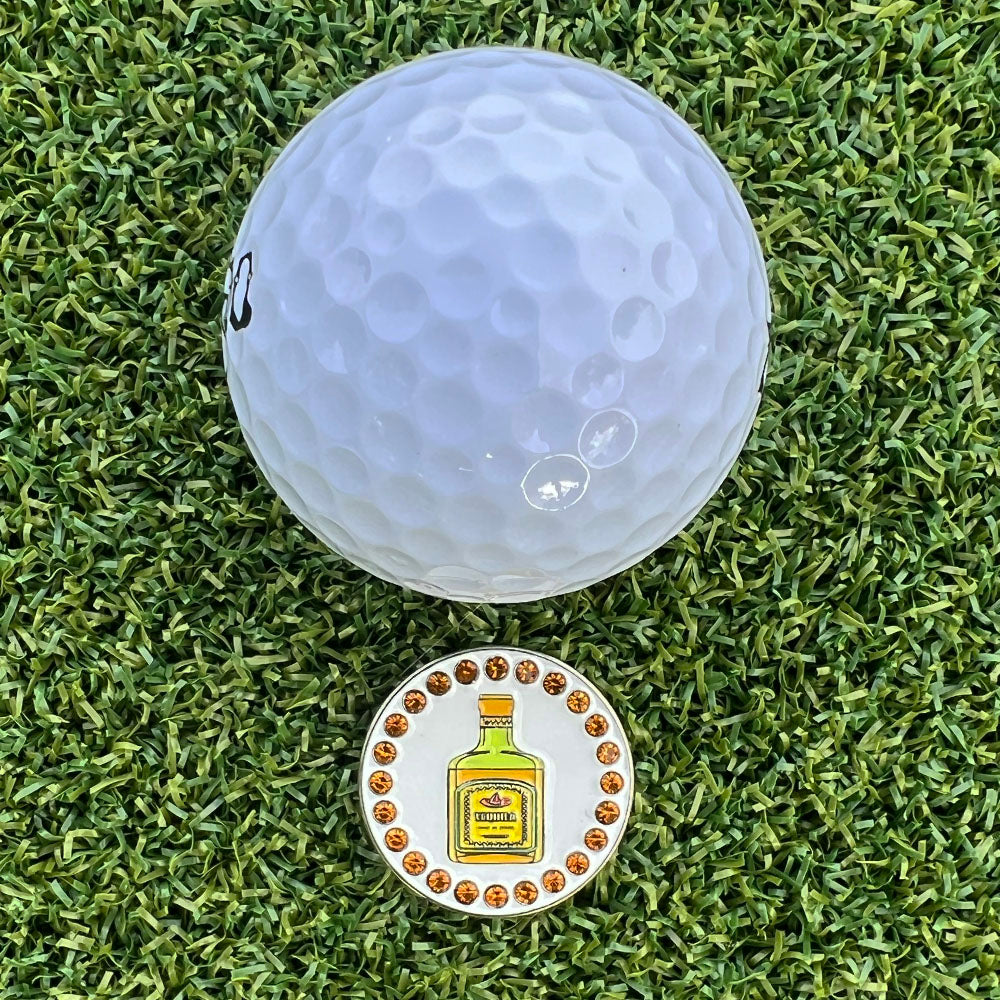 Golf ball marker with a tequila bottle design on grass