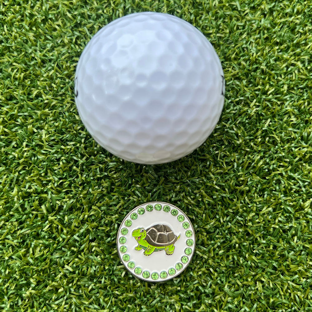 Golf ball and a golf ball marker with a turtle design on grass