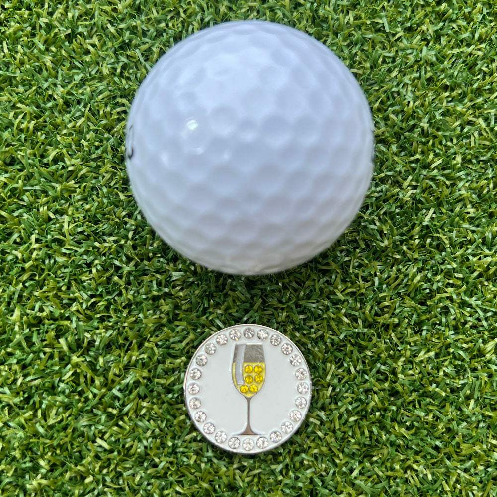 Golf ball on a green grass surface with a glass of white wine ball marker