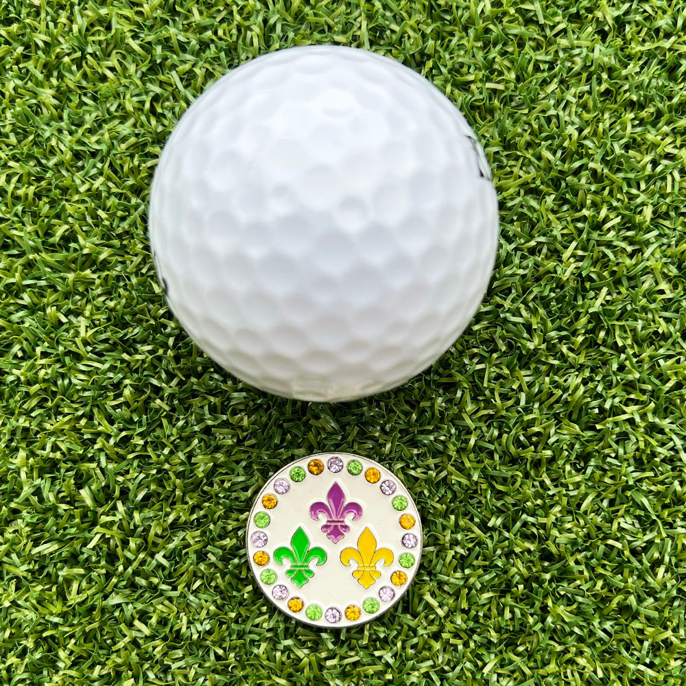 Golf ball on green grass with a colorful golf ball marker featuring fleur de lis design.