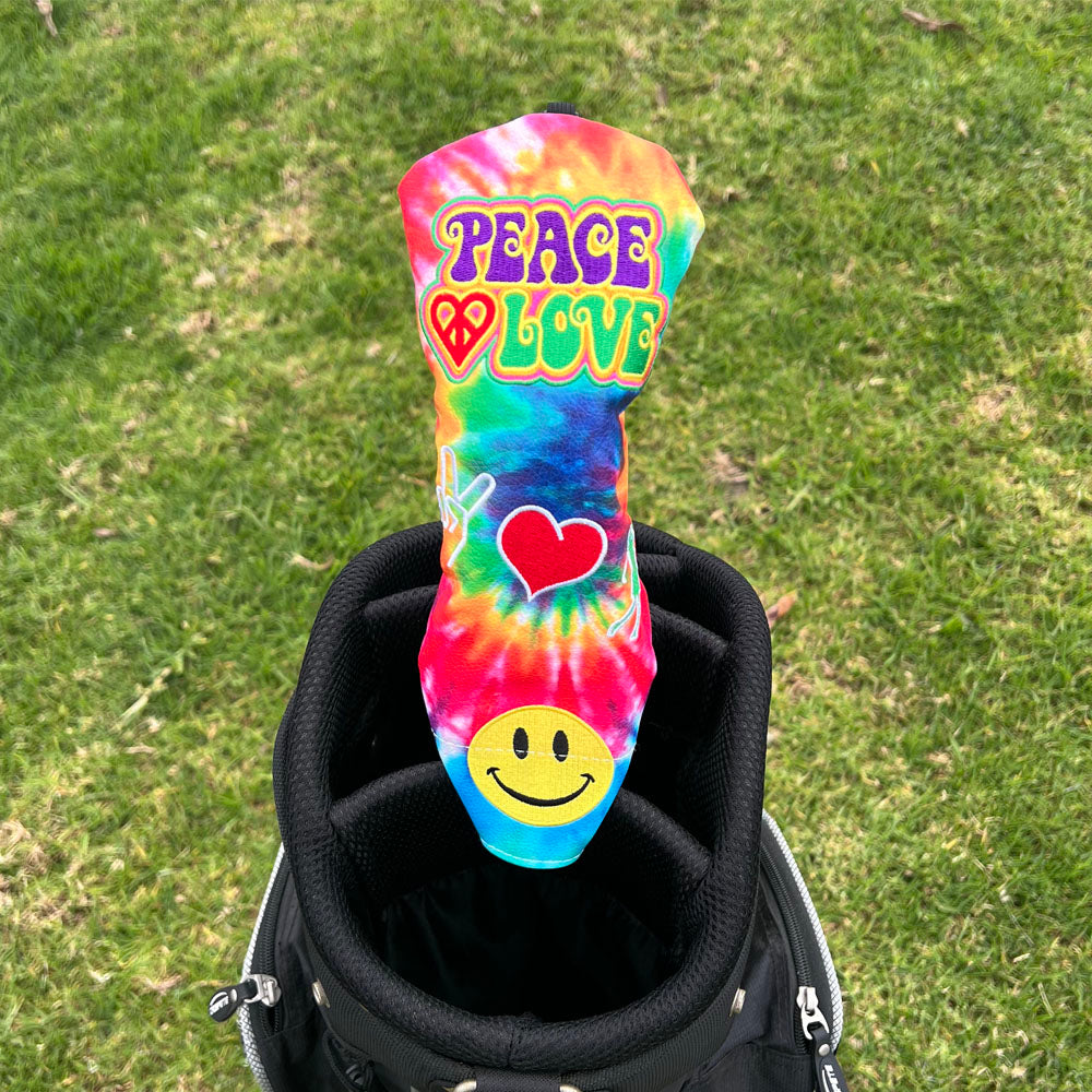Tie-dye golf head cover with 'Peace Love' text and heart symbol on a golf bag.