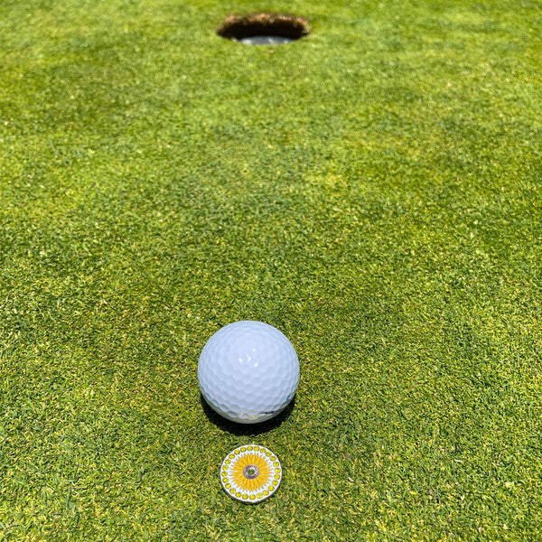 Giggle Golf Bling Sunflower Ball Marker On The Putting Green, Behind A White Golf Ball