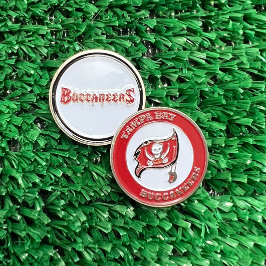 Double sided Tampa Bay Buccaneers golf ball marker on a green artificial turf background. One side shows the white back with red 'Buccaneers' script, and the other shows the front with the red Tampa Bay Buccaneers flag and white background.