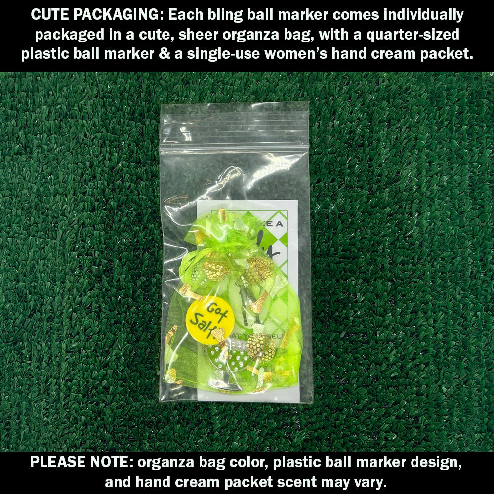 Cute packaging with a margarita ball marker, organza bag, plastic ball marker, and hand cream packet on a green textured background.