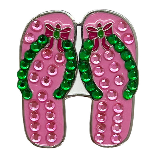 Golf ball marker, pink flip-flop shoes with green straps and rhinestones on a white background