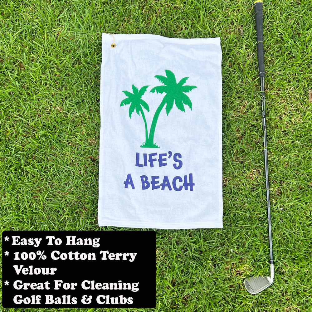 Golf towel with palm tree design and 'Life's a Beach' text on grass, next to a golf club.