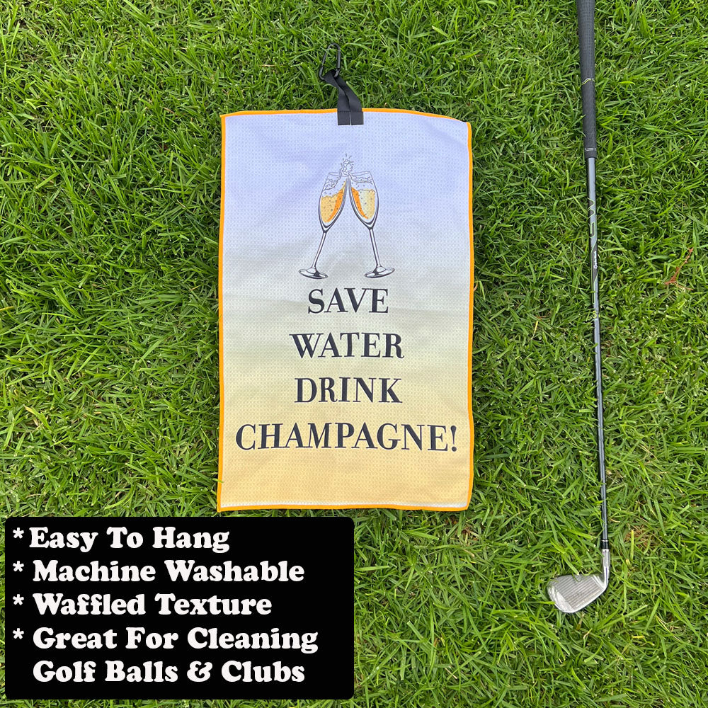 Golf towel with 'Save Water Drink Champagne!' text on grass with golf club