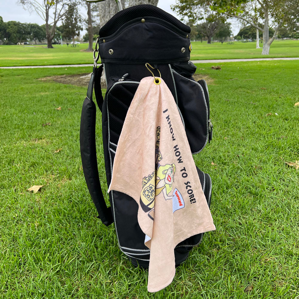 Golf bag with a towel hanging, featuring a cartoon character in leopard print, on a grassy field.