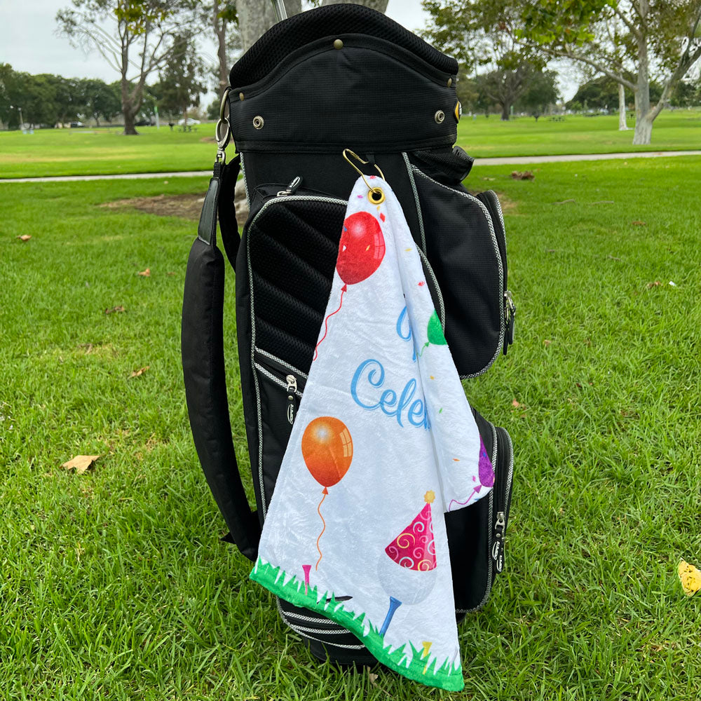 Colorful towel with balloons and text draped over a golf bag on grass