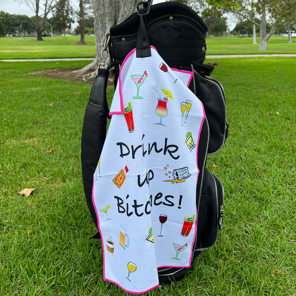 Golf bag with a towel featuring cocktail illustrations and text on a grassy background