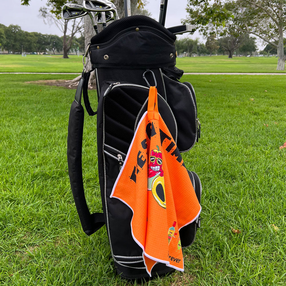 Golf bag with an orange towel featuring a bold Fiesta design on a grassy field.