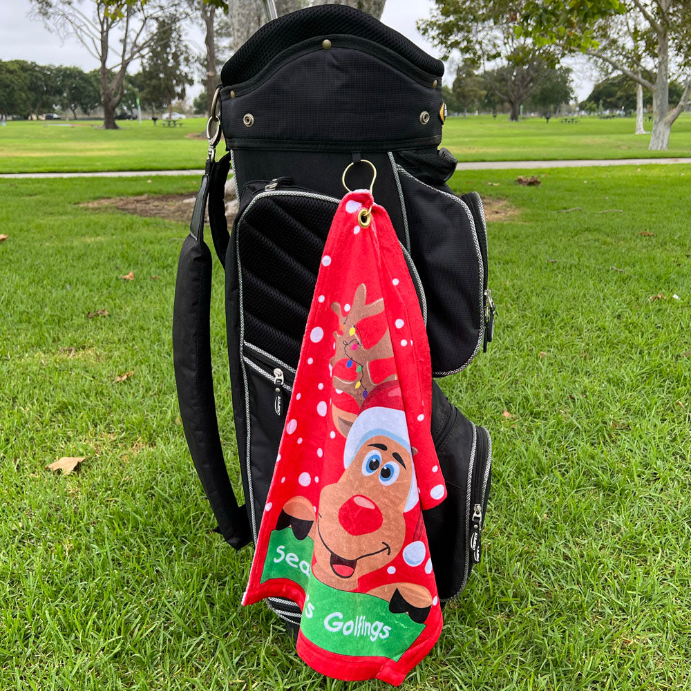 Red towel with cartoon reindeer hanging from a golf bag on grass