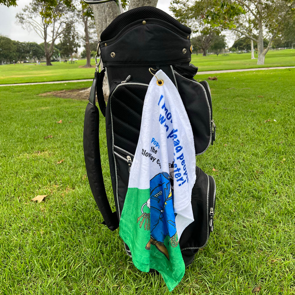 Golf bag with a towel with a cartoon male golf cop design draped over it on a grassy area