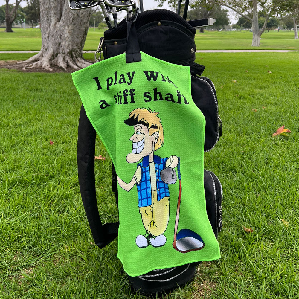 Green golf towel with a funny cartoon character and text on a golf bag on grass