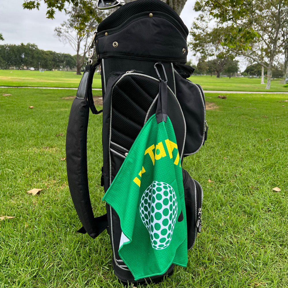 green golf towel hanging on a black bag on grass