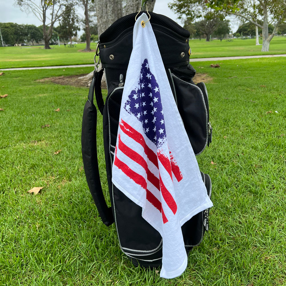 Golf bag with an American flag towel hanging on it on a grassy field