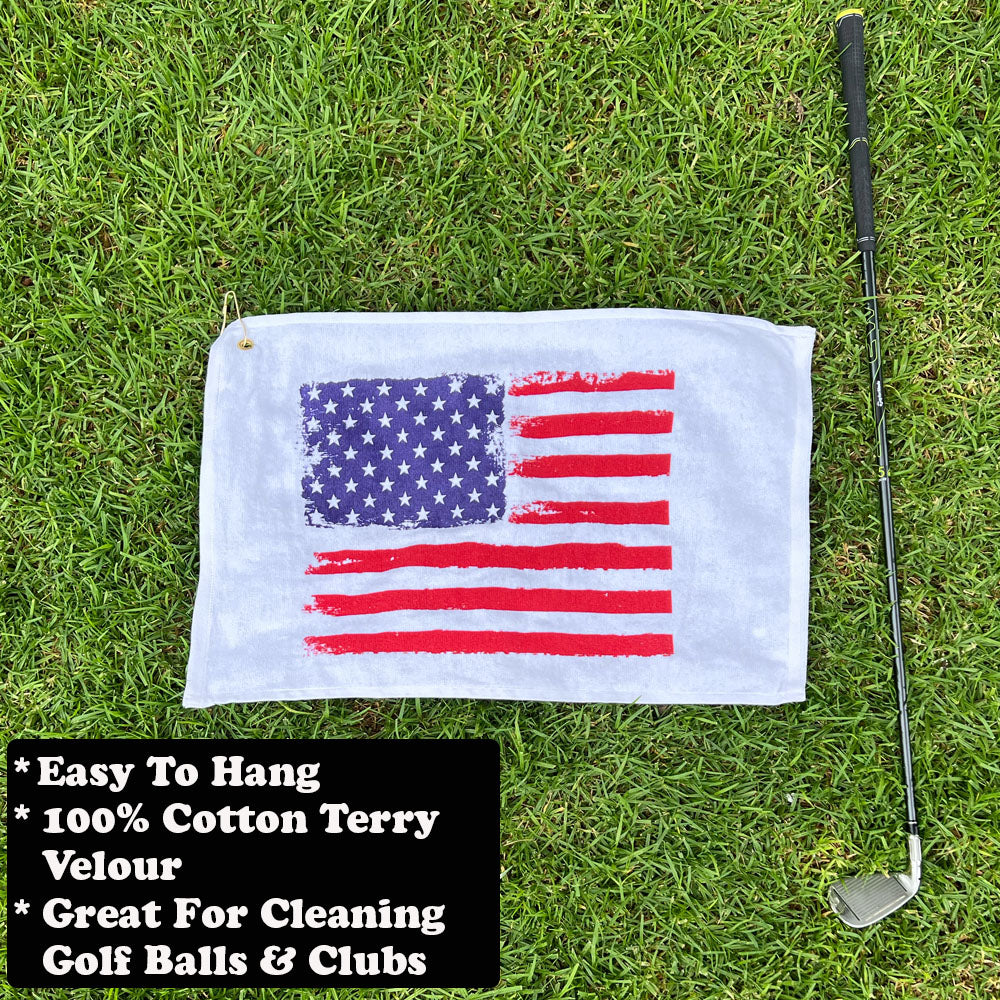 Golf towel with American flag design on grass, next to a golf club.