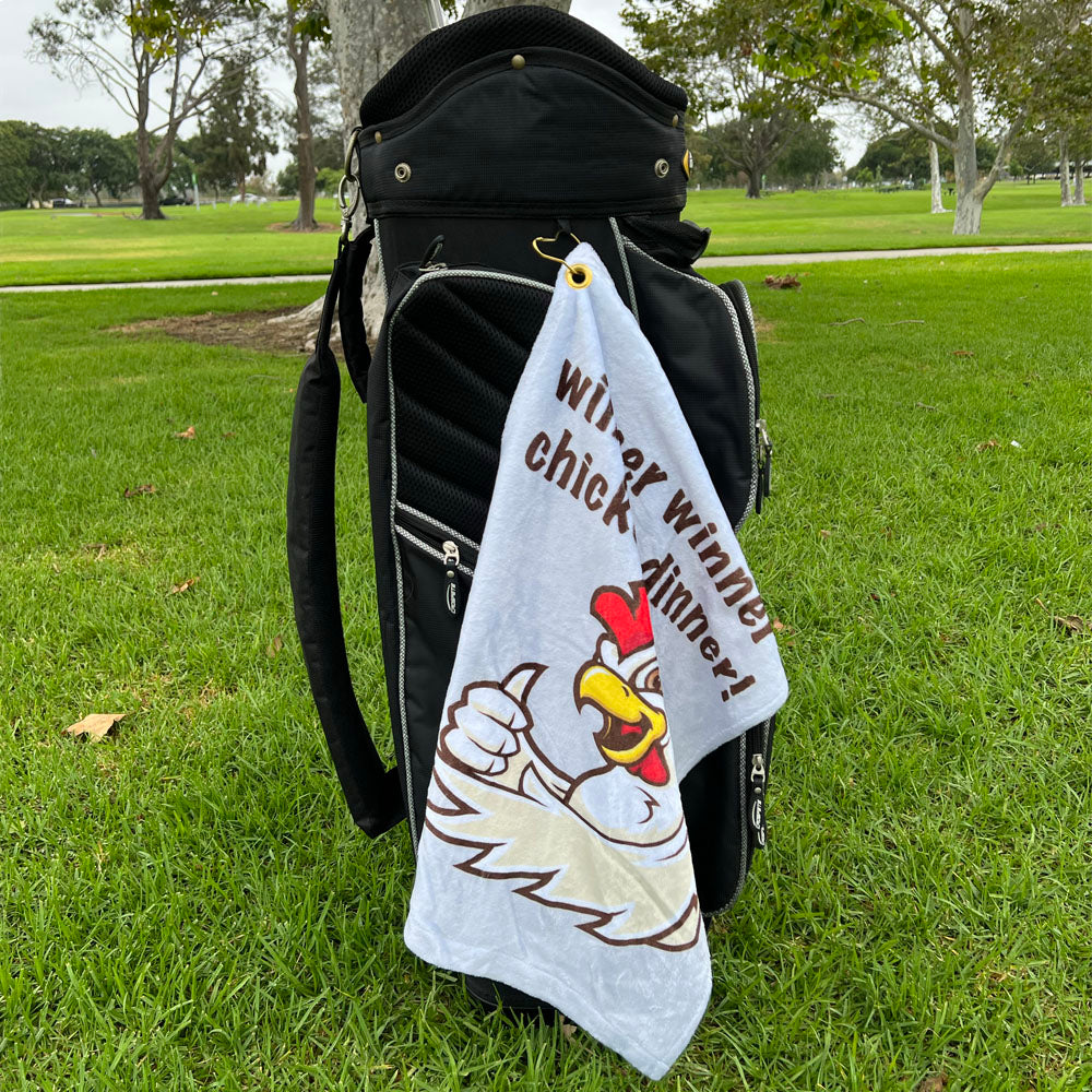 Golf bag with a humorous towel featuring a cartoon chicken on a grassy field